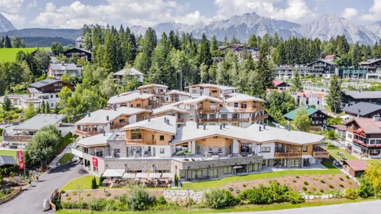 Außenansicht der AlpenParks Apartments & Chalets Alpina in Seefeld in Tirol im Sommer, umgeben von grüner Natur und Tiroler Bergen.